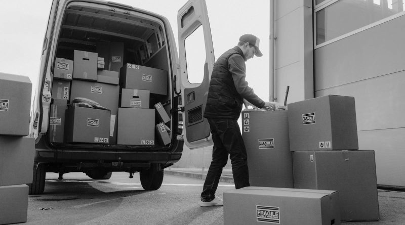 Delivery driver unloads packages from a van, organizing shipments outdoors.