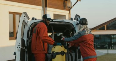Two cleaners in red uniforms load a vacuum into a white van outdoors.