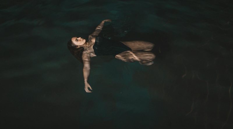 A woman peacefully floats on her back in a dark, serene swimming pool at night, exuding relaxation.